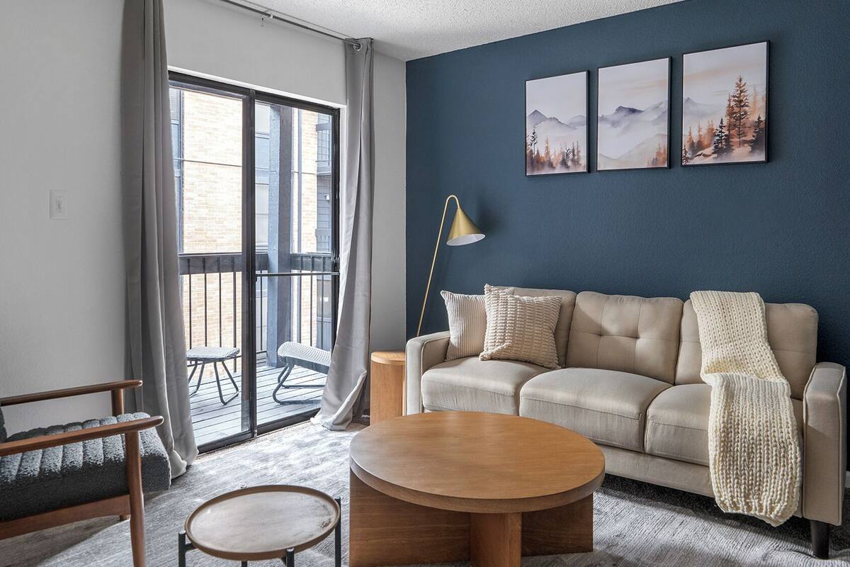 Un salon comprenant un canapé, une table basse ronde, un fauteuil et un balcon donnant sur un immeuble.