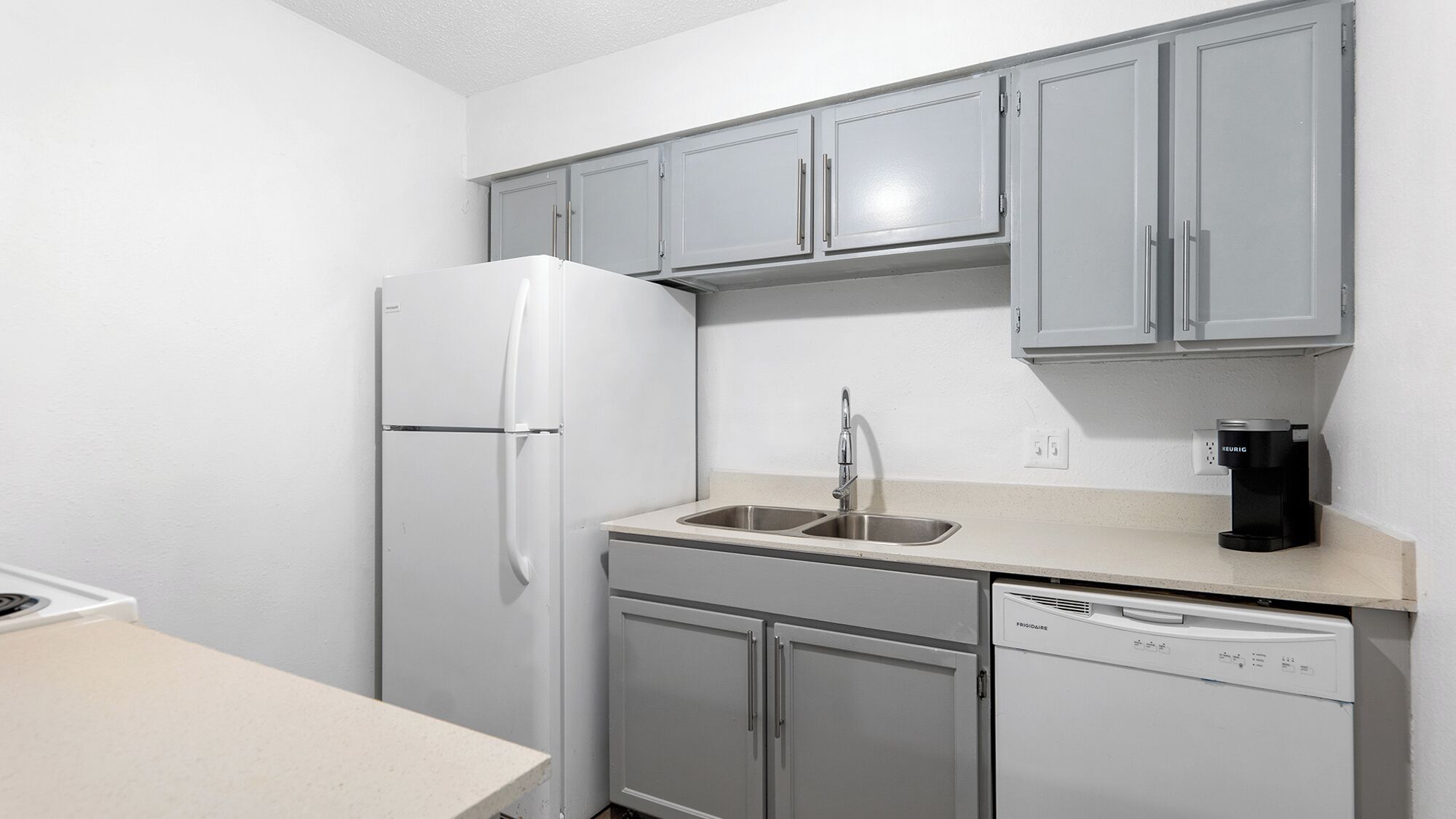 A compact kitchen with a white refrigerator, a sink with a faucet, a coffee maker, and a dishwasher.
