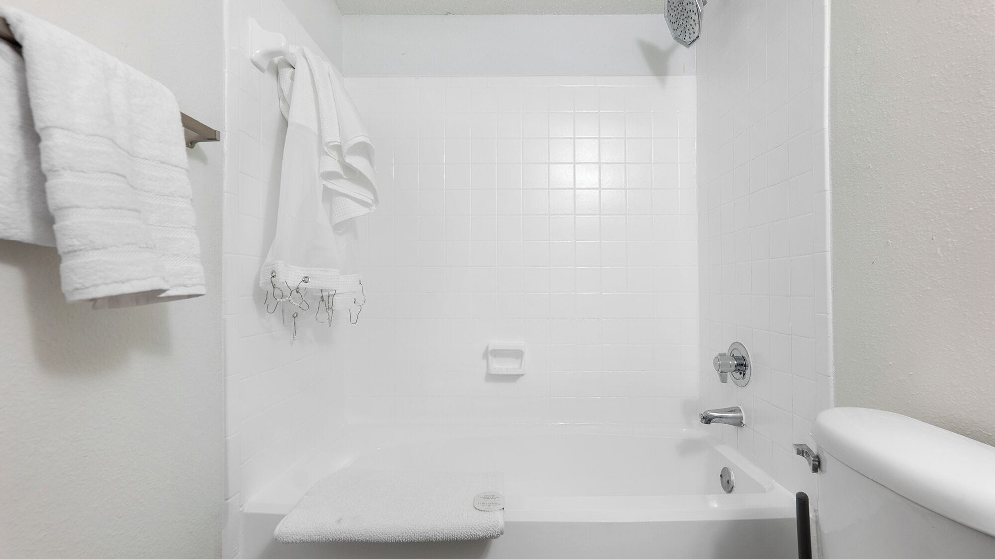 A white bathroom with a bathtub, a shower, and a toilet. There are towels hanging on a rack.