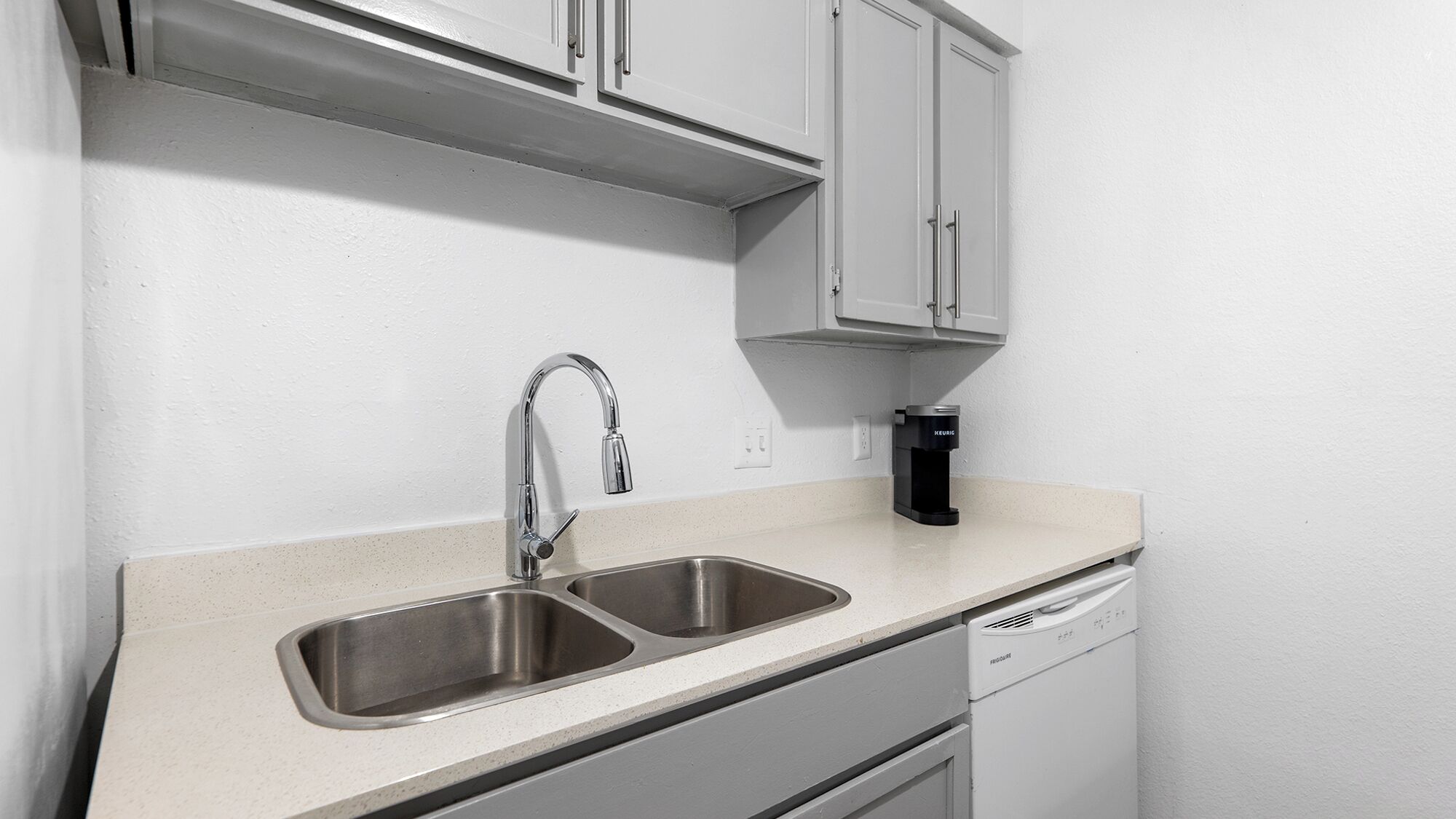 A kitchen with a double sink, a coffee maker, and a dishwasher.