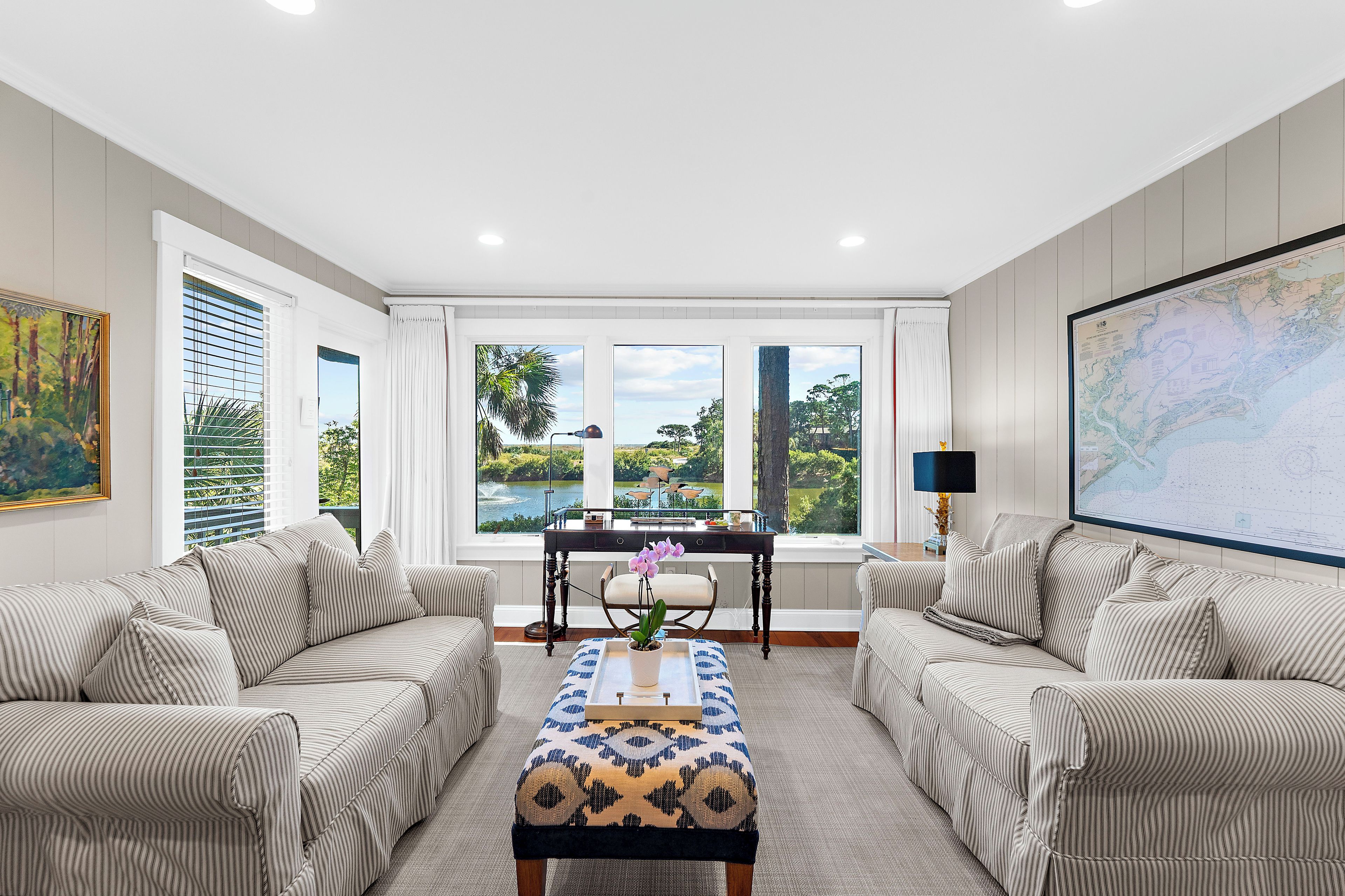 A room with two sofas, a coffee table, a desk, and large windows with a view of greenery and a lake.