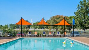 A swimming pool with three orange canopies, lounge chairs, and a clear blue sky. - Landing Tulsa near Woodland (Tulsa)
