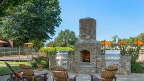 An outdoor seating area with Adirondack chairs, a stone-built pizza oven, and a grill. - Landing Tulsa near Woodland (Tulsa)