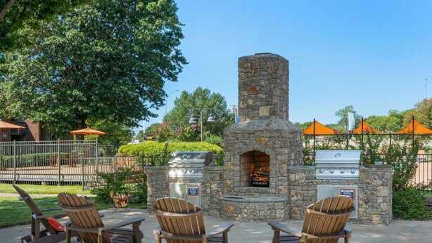 Un espace extérieur aménagé avec des chaises Adirondack, un four à pizza en pierre et un barbecue.