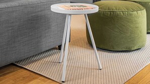 Moderni olohuone, jossa on harmaa sohva, pyöreä valkoinen sivupöytä, vihreä jalkarahi, seinälle asennettu musta televisio ja pieni kasvi kaapin päällä.