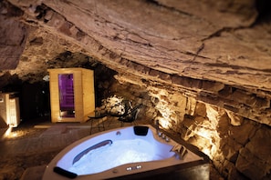 A spa area with a hot tub, wooden cabin, and stone walls.
