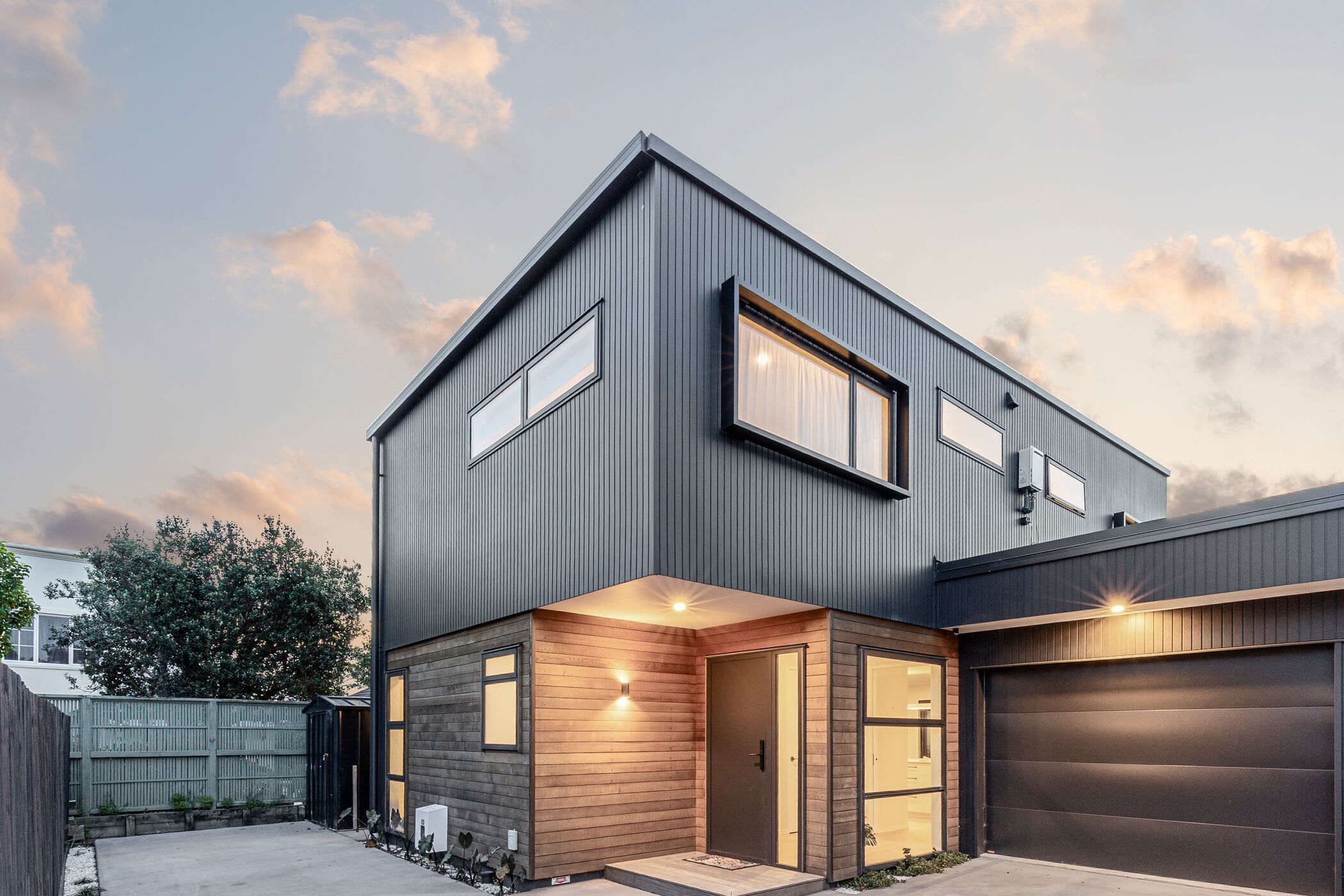 A modern two-story house with a dark exterior, a wooden front porch, and a garage.