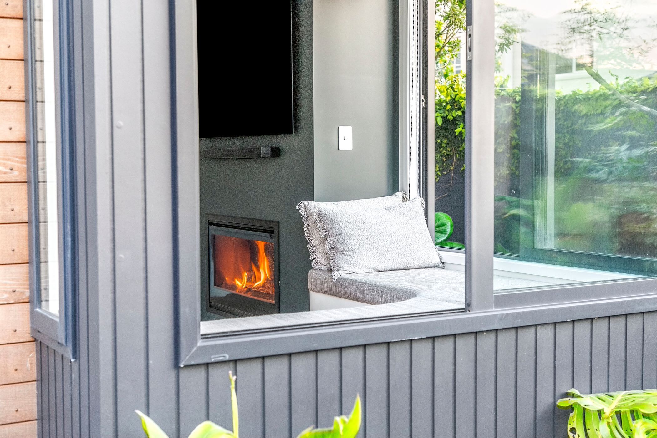 A modern outdoor seating area with a built-in fireplace, a comfortable bench, and a glass enclosure.