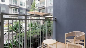 A balcony with a metal railing, a small round table, and two wicker chairs. - Landing Furnished Apartments - Old East (Dallas)