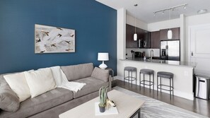 A modern living room with a grey sofa, a white lamp, and a coffee table with a plant. - Landing Furnished Apartments - Old East (Dallas)
