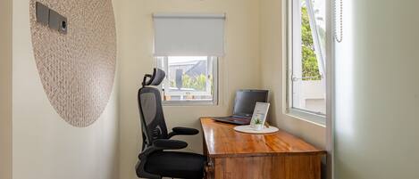 A small office space with a wooden desk, a black office chair, a laptop, and a window with a view of the outside.