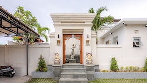 A modern building with a central entrance, steps leading up to it, and two statues on either side. - Cove Dharma Kencana (Kutuh)