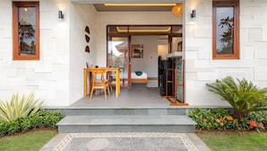 A modern house with a wooden door, a small dining area with a table and chairs, and a bed visible through a glass door. - Cove Dharma Kencana (Kutuh)