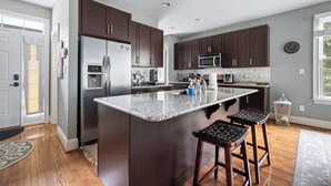 Une cuisine moderne avec des meubles de couleur sombre, des appareils en acier inoxydable, un îlot en granit et un plancher en bois.