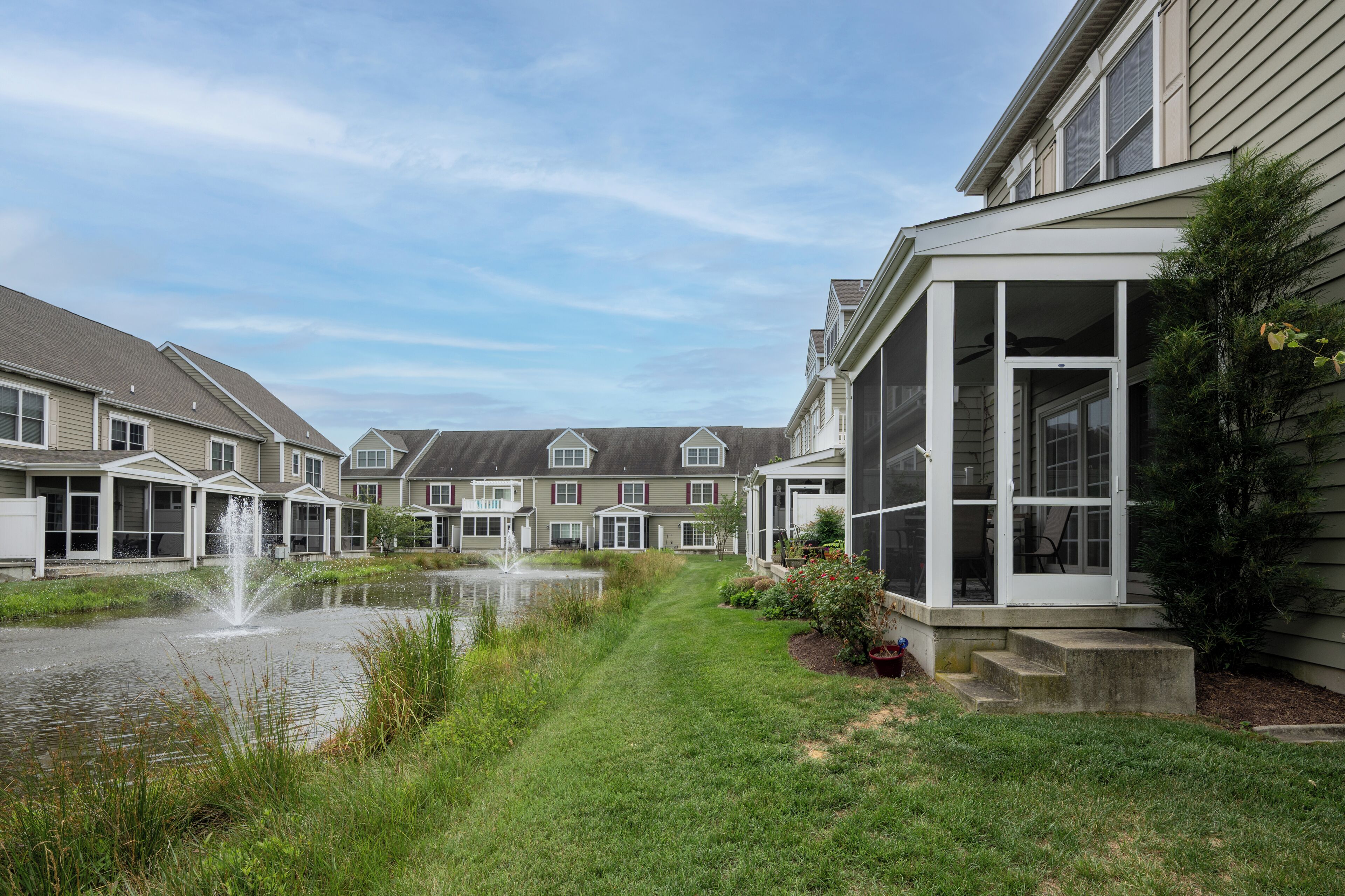A residential area with a pond, houses with balconies, and a clear sky.