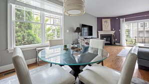 Un coin repas avec une table en verre, des chaises blanches, une cheminée et un téléviseur.