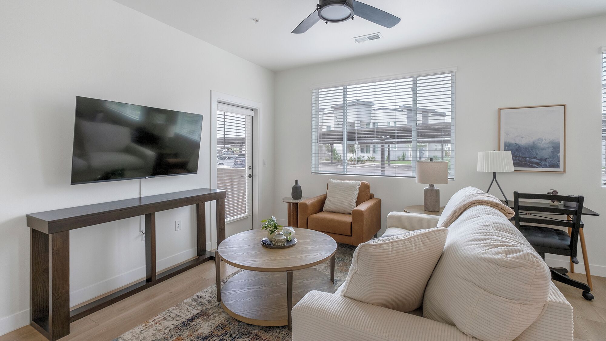Een moderne woonkamer met een flatscreen-televisie, een bank, een salontafel en een eethoek met een stoel en een lamp.