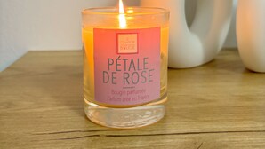 Una vela encendida en un recipiente de vidrio con una etiqueta que dice "Pétale de Rose".