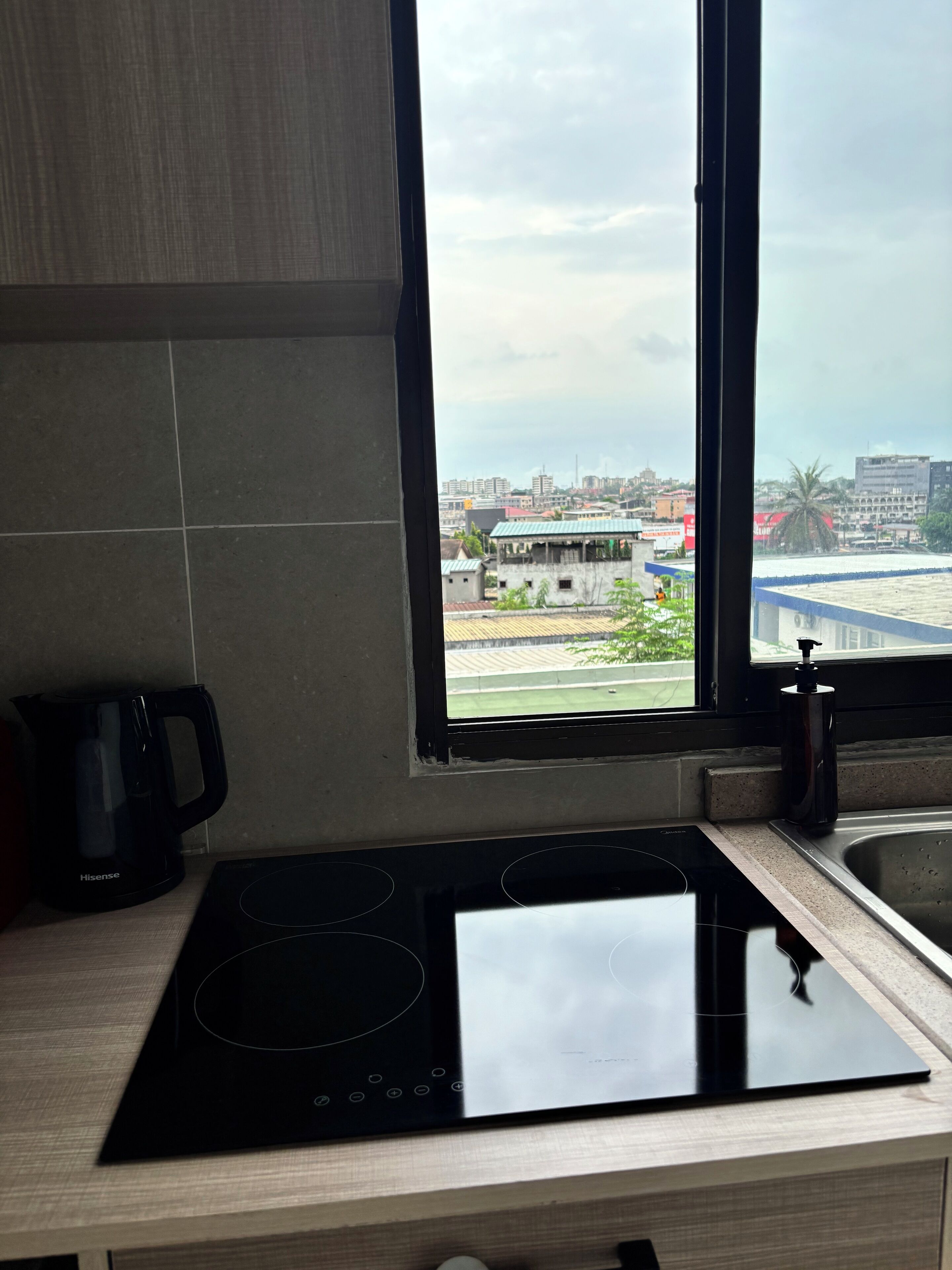 Une cuisine dotée d’une plaque de cuisson à induction noire, d’une machine à café et d’une fenêtre donnant sur un paysage urbain.
