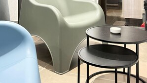 Una habitación moderna con una silla verde curva, una silla azul y una pequeña mesa redonda con un plato blanco.