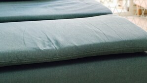 Un letto con materasso e cuscini grigi, una parete bianca e un balcone con ringhiera.