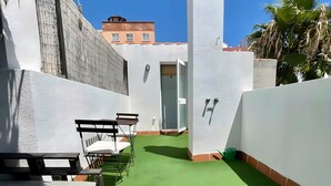 Patio esterno con tavolo in legno, prato sintetico verde e parete bianca con bocchetta di ventilazione.