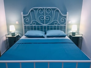 A bed with a metal headboard, two bedside lamps, and a blue bedspread.
