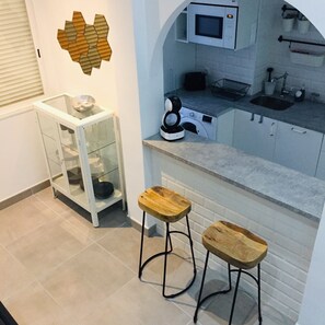 A compact kitchen with a microwave, sink, and a glass cabinet. There are two wooden stools and a decorative wall piece.