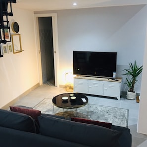 A living room with a sofa, a coffee table, a TV on a cabinet, a door, and a plant.