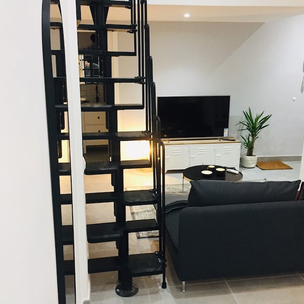 A modern living room with a black staircase, a flat-screen TV, a sofa, and a potted plant.