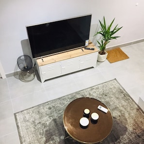 A living room with a flat-screen TV, a potted plant, a round coffee table with three cups, and a remote control.