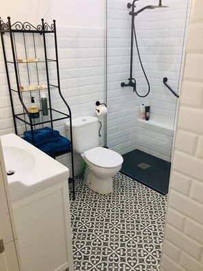 A bathroom with a white toilet, a black metal shelf with toiletries, a patterned floor, and a shower area.