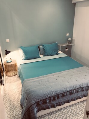 Une chambre à coucher avec un lit, une lampe de chevet, une petite table ronde et une étagère fixée au mur.