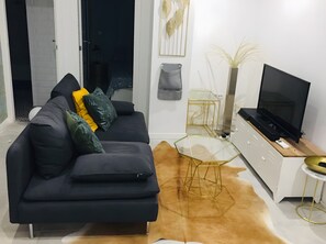 A modern living room with a black sofa, a glass coffee table, a TV on a stand, and a decorative vase.