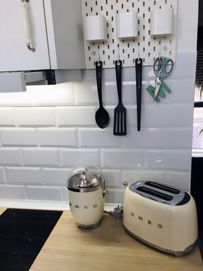 A kitchen with a white backsplash, a wall-mounted pegboard with kitchen utensils, a juicer, and a toaster.