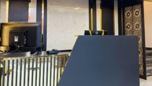 Egy előtér, melyben fekete recepciós pult, márványfal és díszes ajtó található.