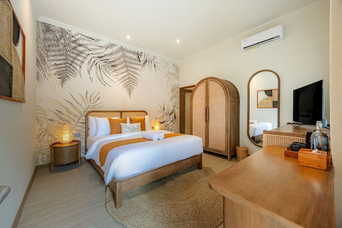 A hotel room with a large bed, a wooden desk, a TV, and a wall with a leaf pattern.