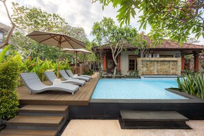 A swimming pool with lounge chairs and umbrellas, surrounded by tropical plants and a wooden deck. - Cove Jivva Nattaya (Denpasar)