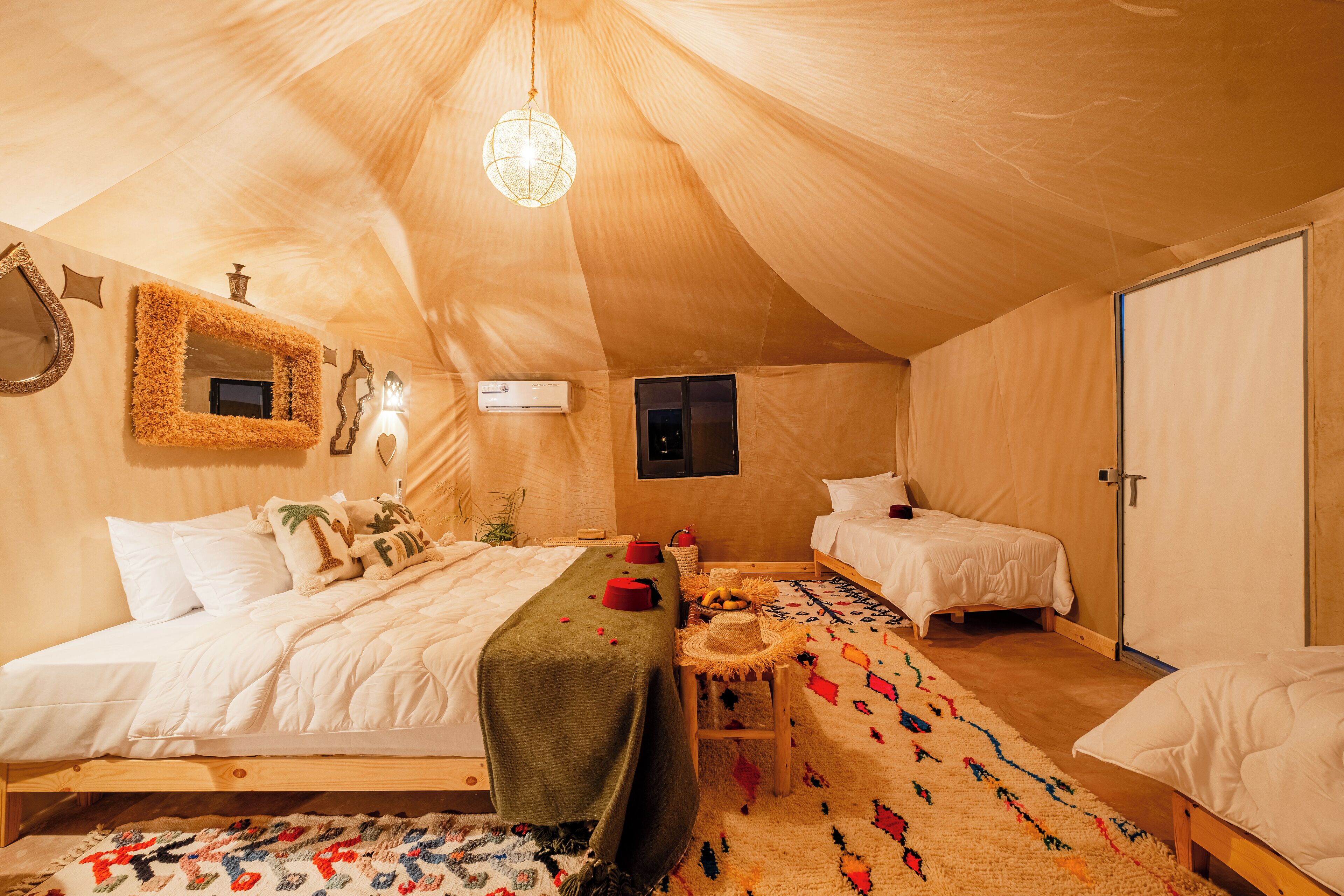 Een tentachtige kamer met twee bedden, een tafeltje en een hanglamp.