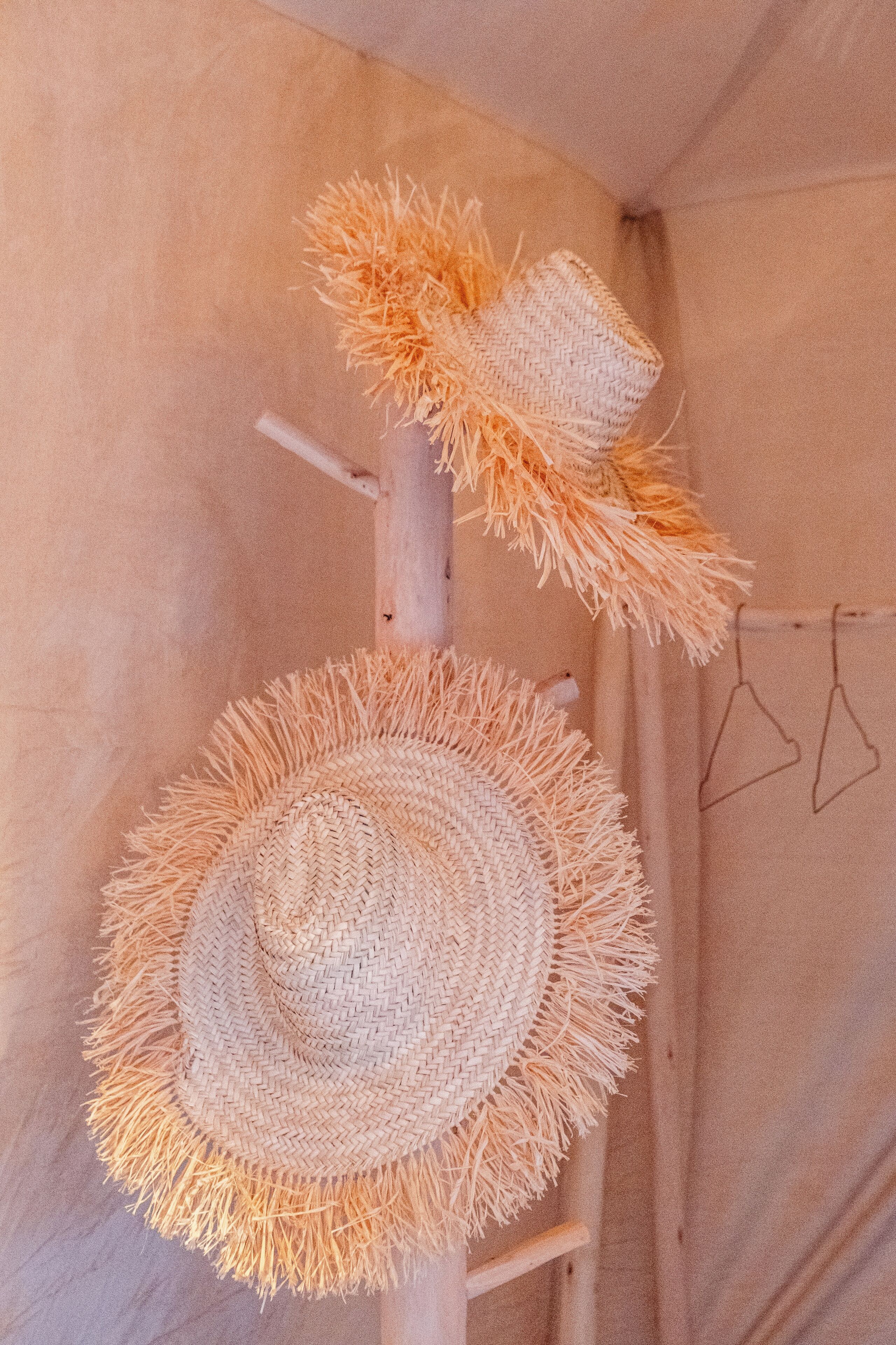 A straw hat hanging on a wooden pole in a tent-like structure.