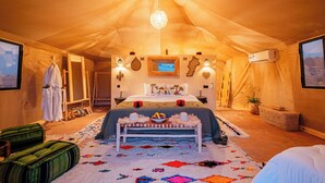 A tented room with a bed, a chandelier, a television, and a view of the desert outside.