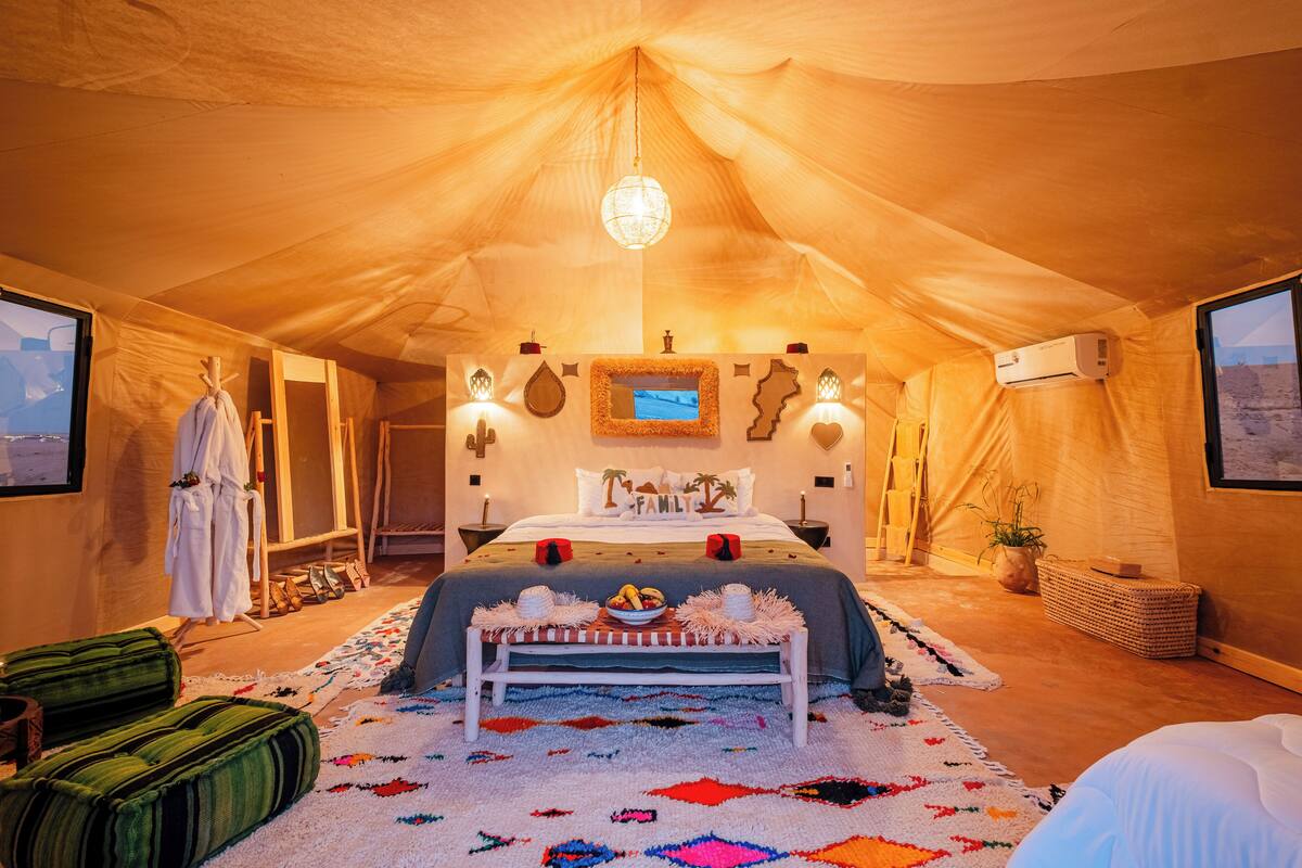 Ein Zeltraum mit Bett, einer Kandelaber, einem Fernseher und Blick auf die Wüste.