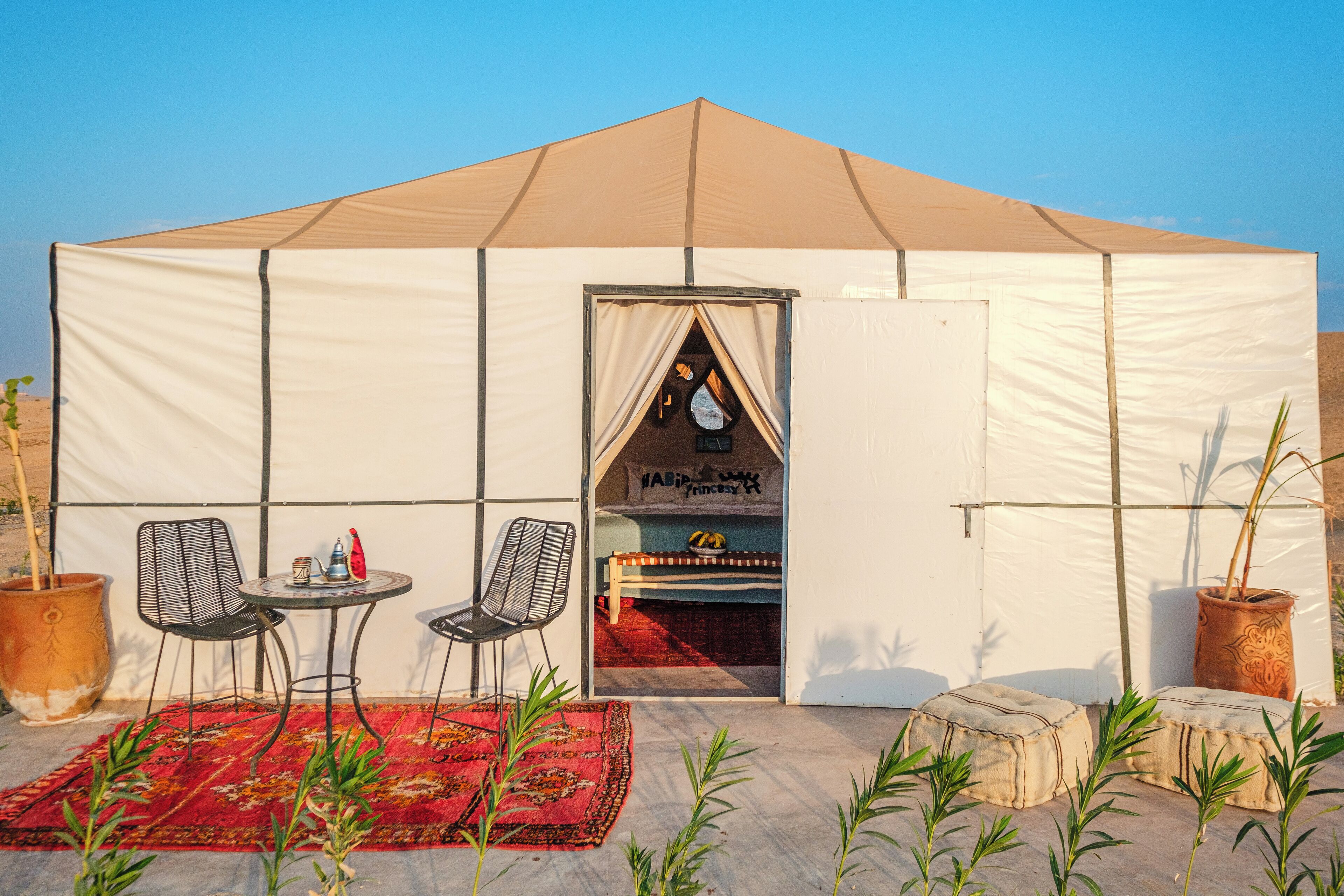 A tent with a bed, two chairs, a small table, and a red rug.