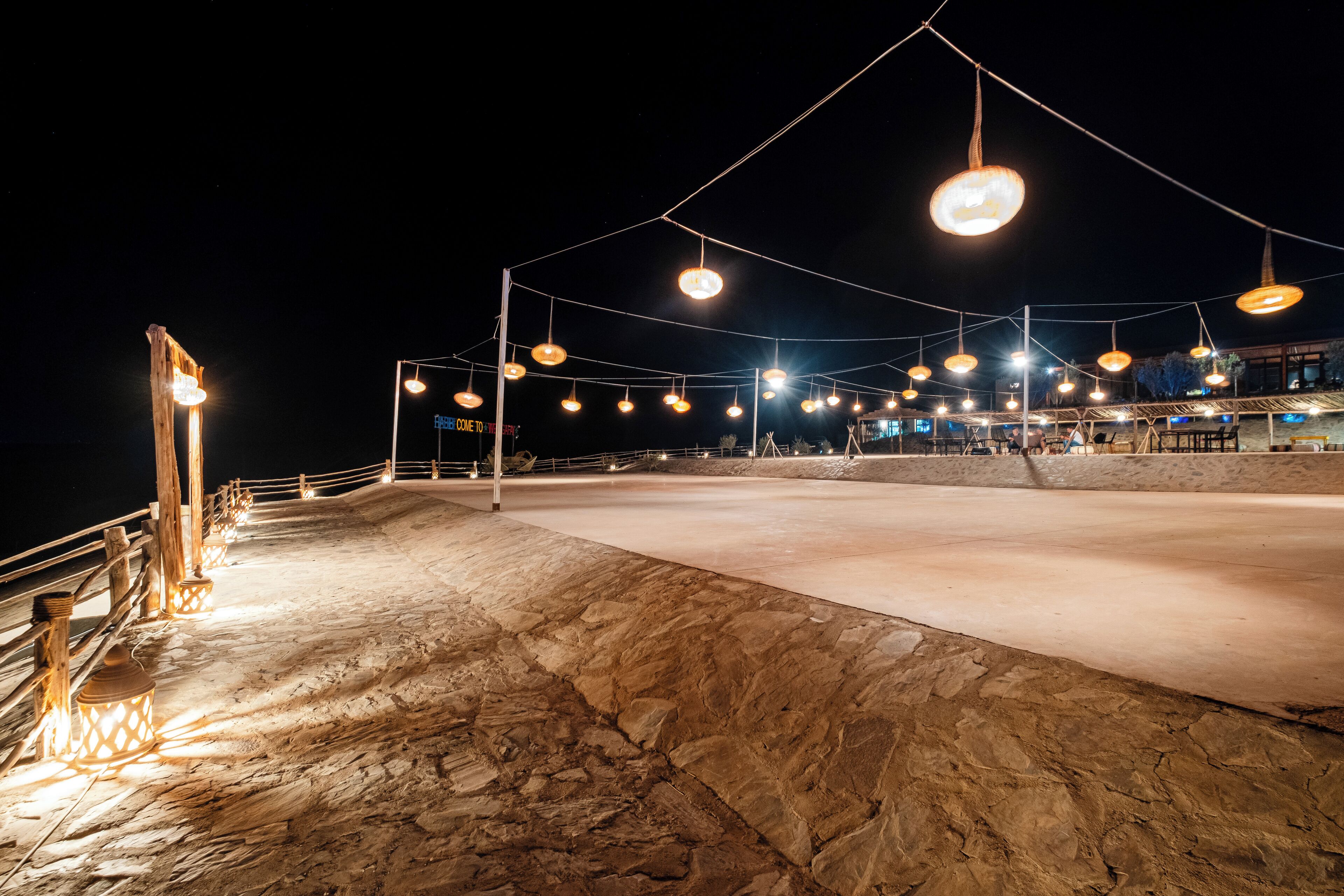 Un espacio exterior con piso de piedra y barandilla, iluminado por luces colgantes.