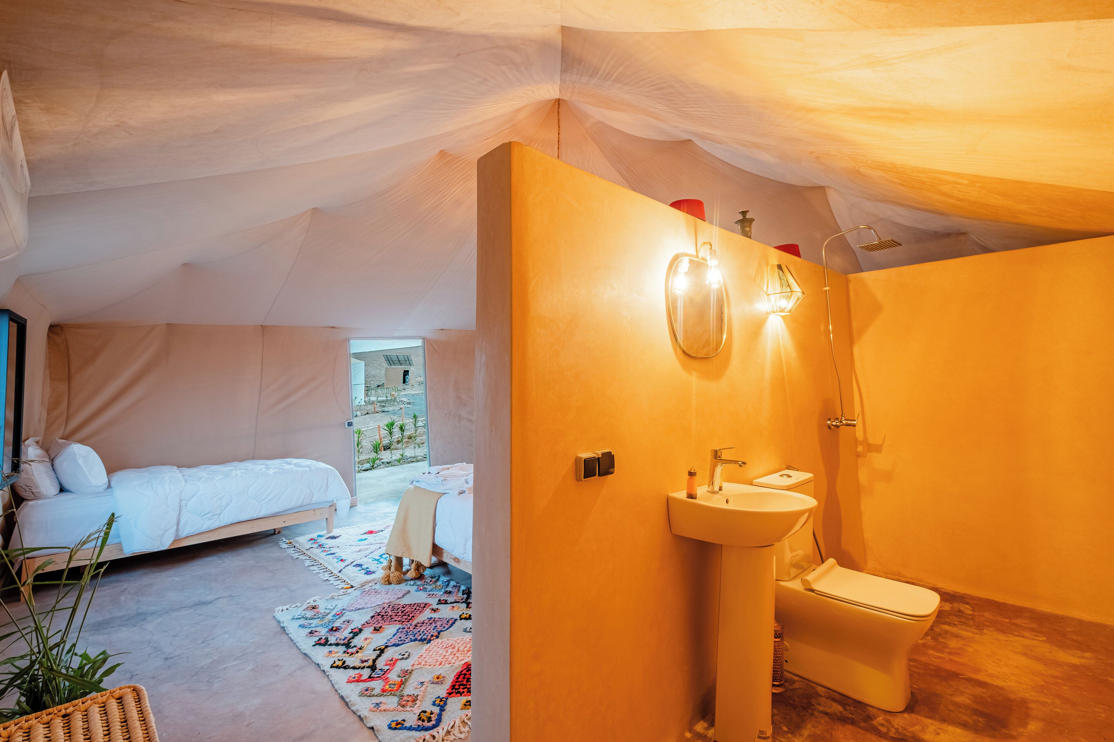 A tented accommodation with a bed, a sink, and a toilet.