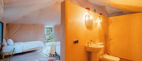 A tented accommodation with a bed, a sink, and a toilet.