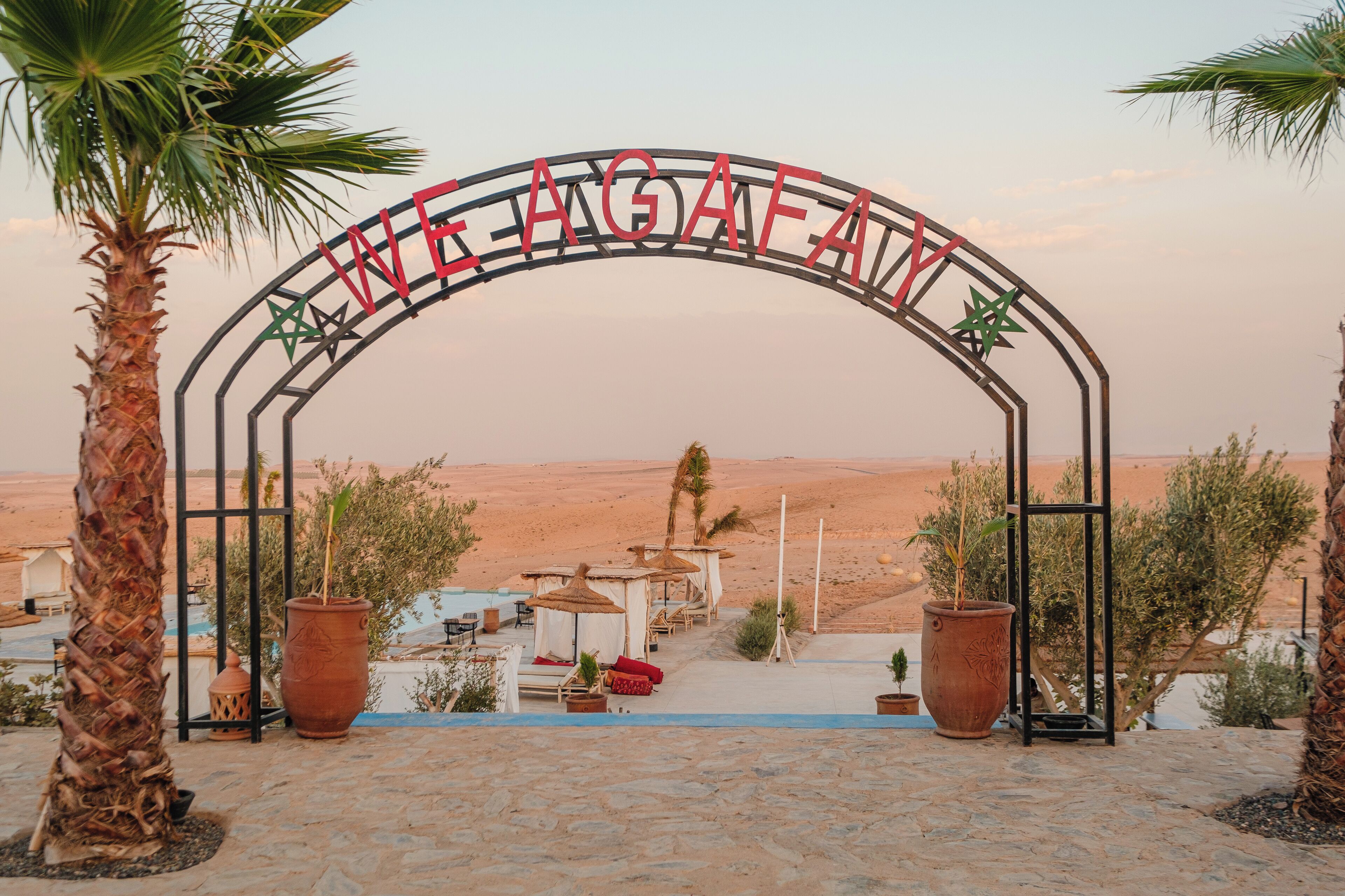 An archway with the text "WE AGAFAI" and palm trees in the foreground.