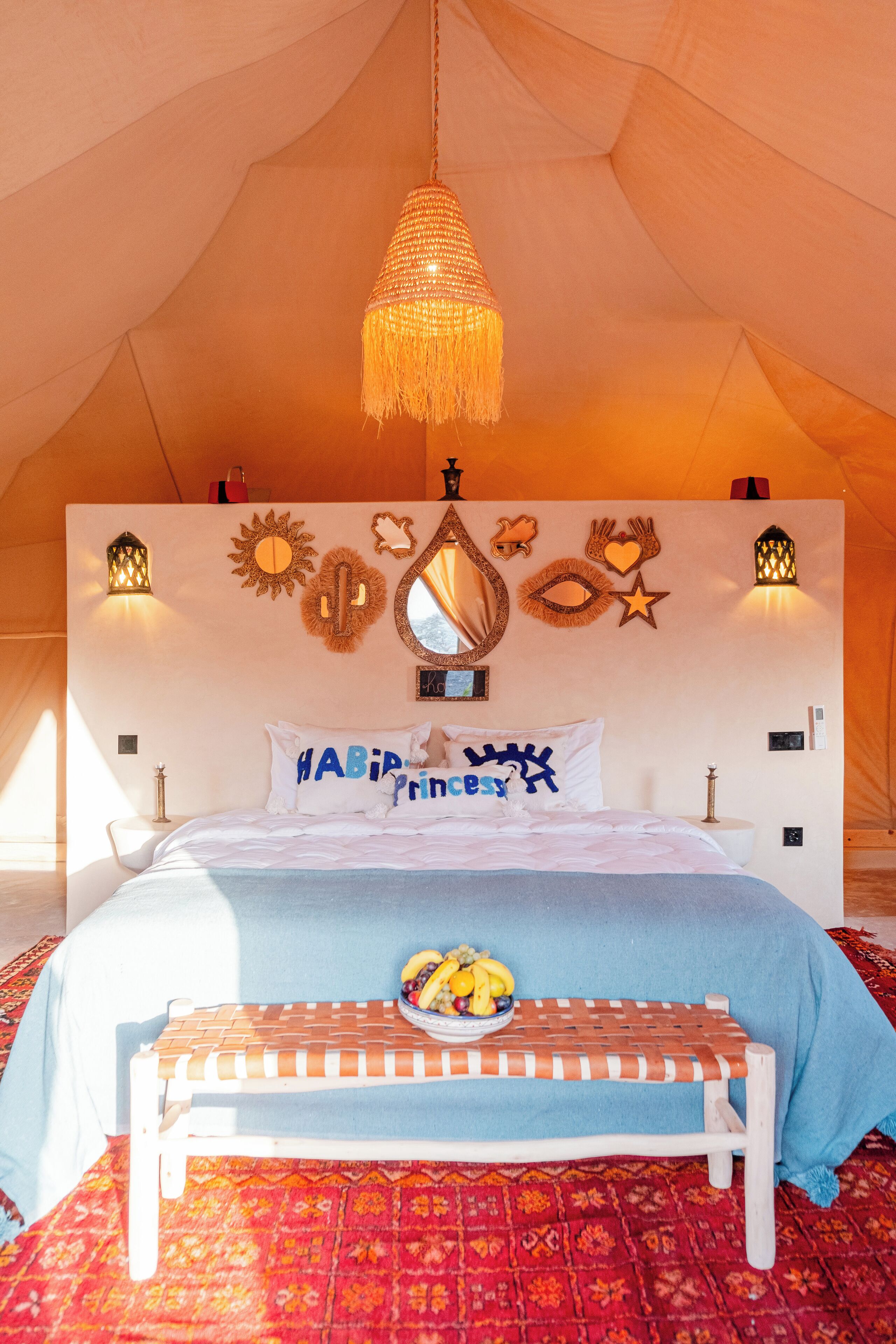 Habitación tipo alojamiento en tienda con una cama, lámparas de noche, una lámpara colgante, un espejo y adornos en la pared.