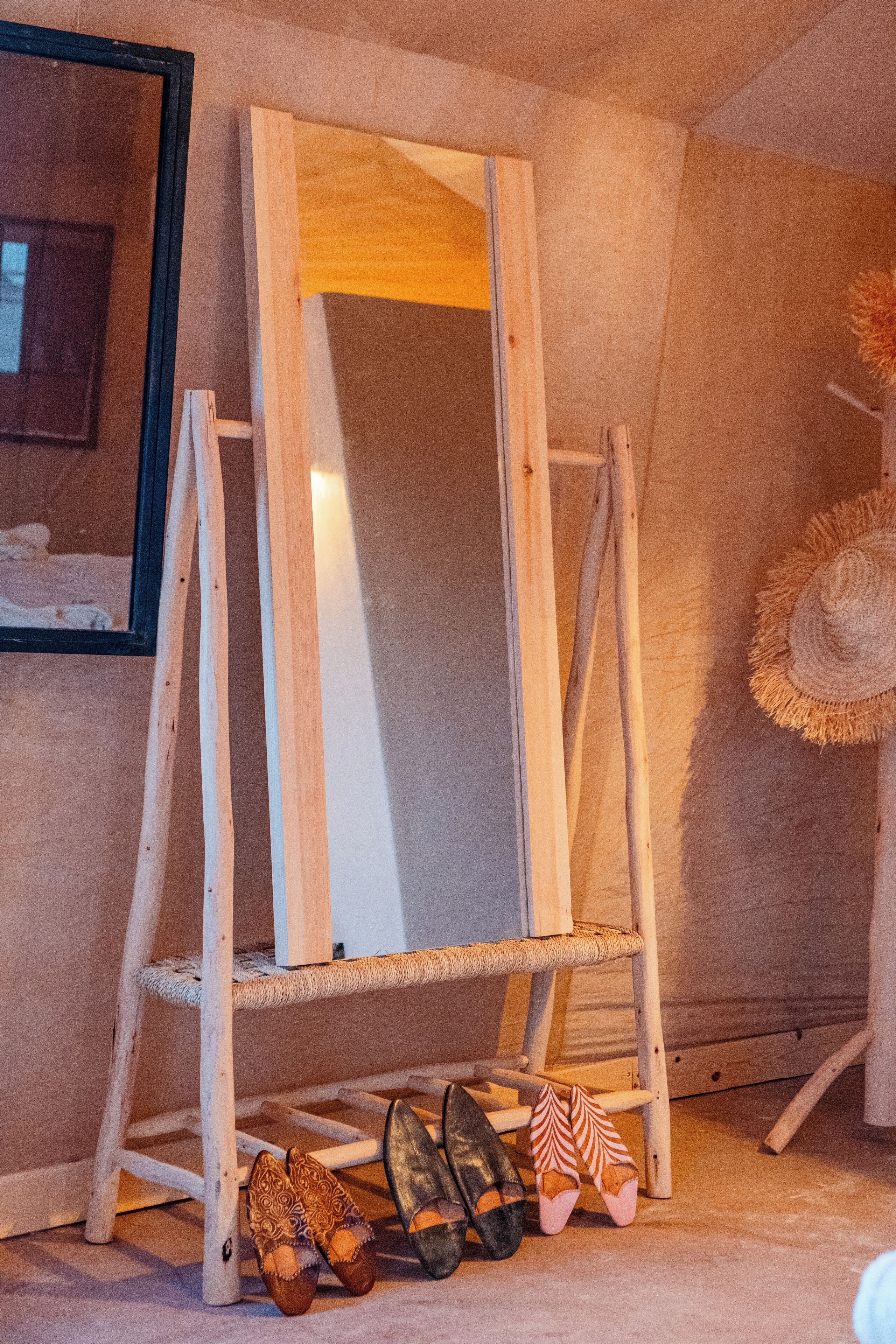A wooden ladder with a mirror, a straw hat, and a pair of shoes on the floor.