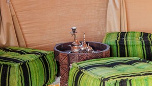 A room with two green striped ottomans, a small table with a decorative item, and beige curtains.
